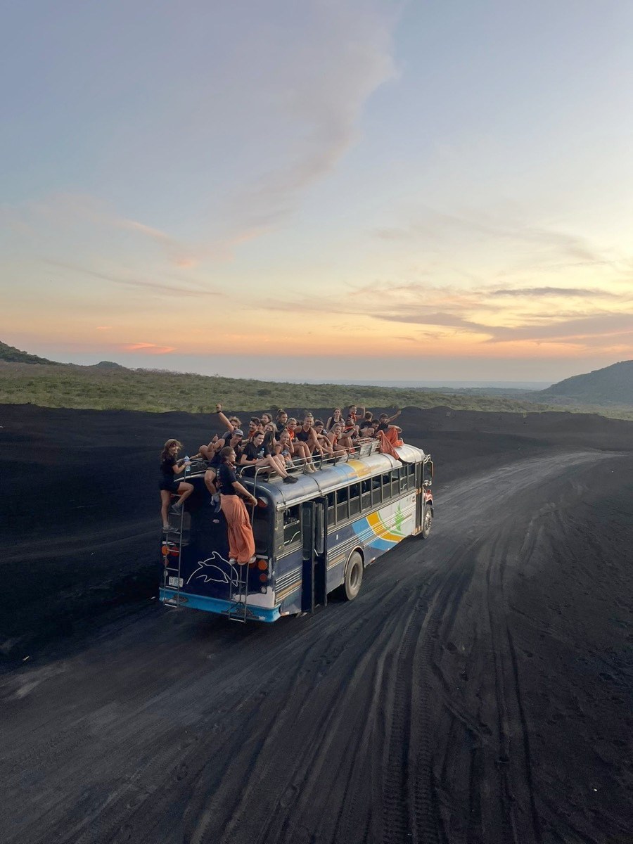 A crowded bus crossing black sand at sunset