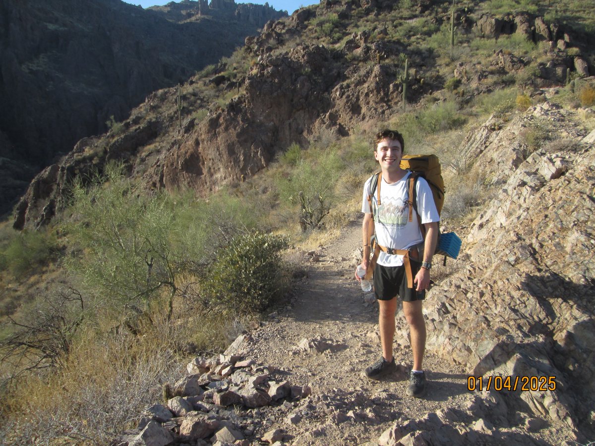 On a rocky canyon trail among saguaros, pack on, grinning