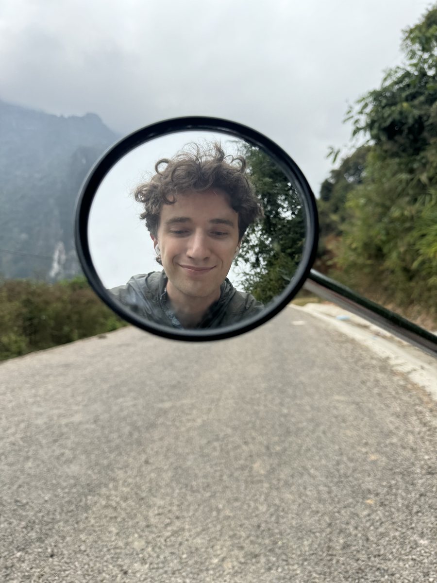 My face in a scooter mirror on a misty mountain road